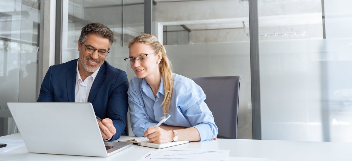 Mature mentor senior leader man showing young woman employee project on laptop in office